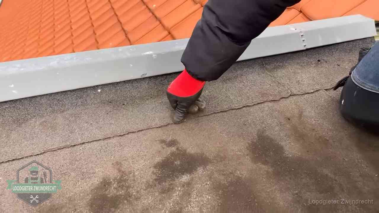 Vakman wijst een naad met vochtplekken aan op een bitumen plat dak in Zwijndrecht