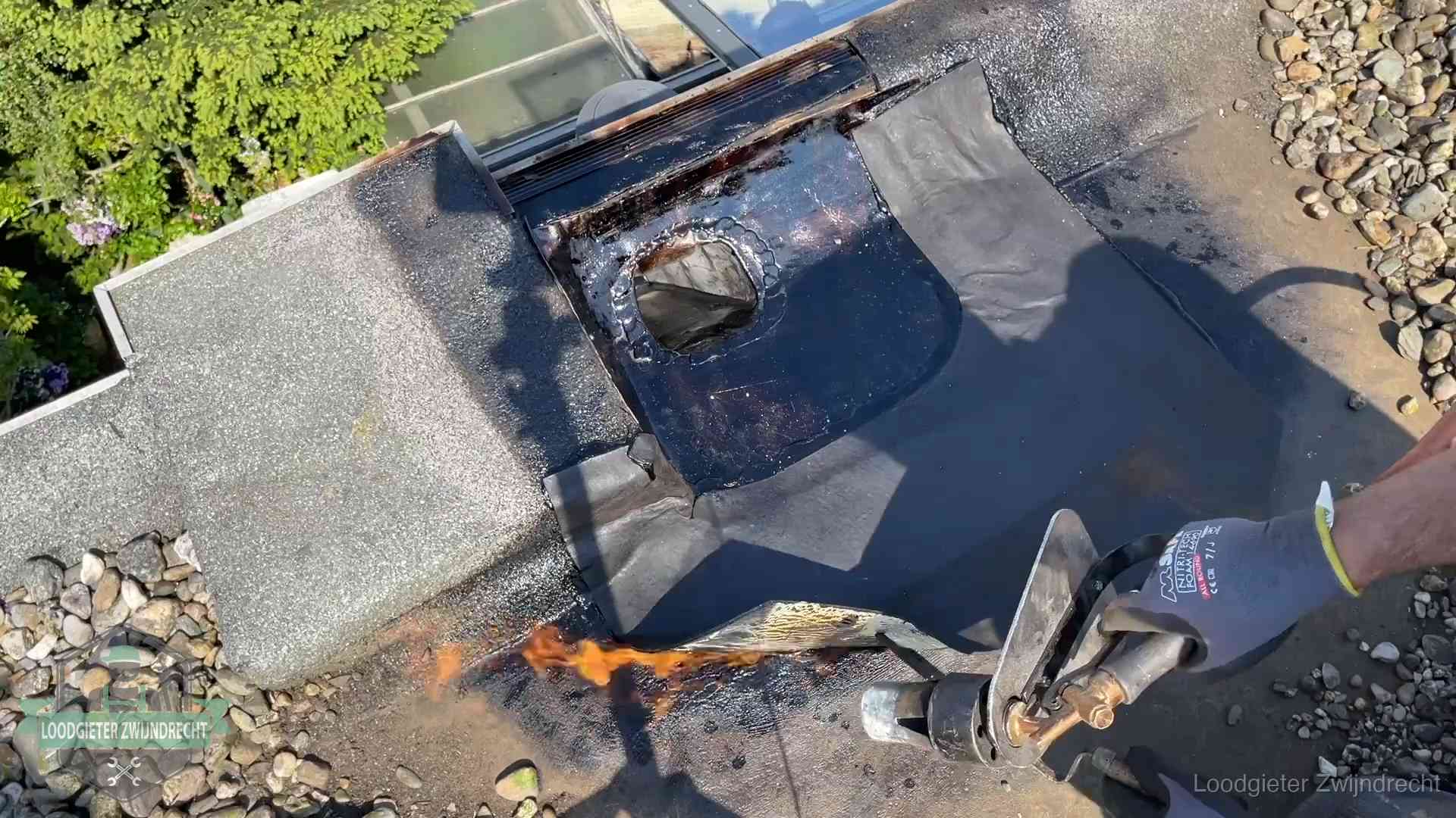 Dakdekker brandt bitumen rond een doorvoer tijdens een daklekkage-reparatie in Zwijndrecht