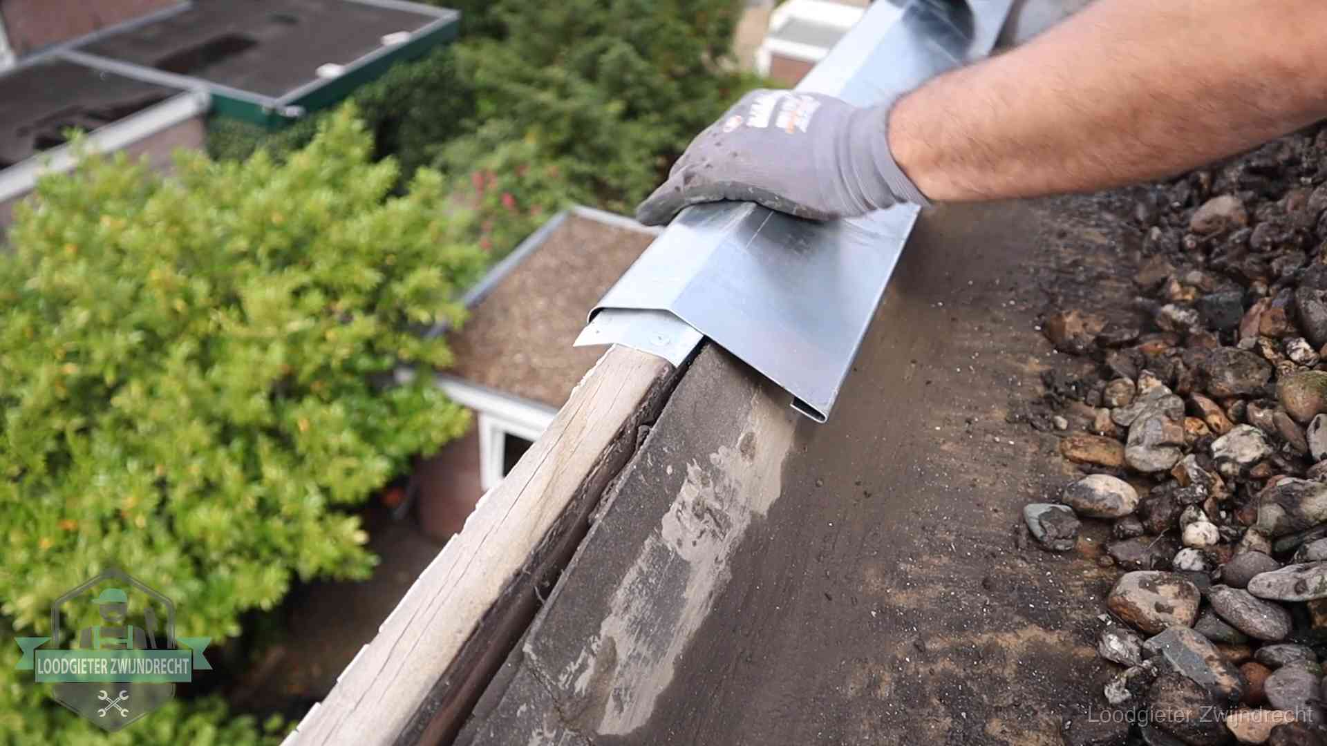 Dakdekker plaatst een zinken deklijst op een dakrand met uitzicht over een woonwijk in Zwijndrecht