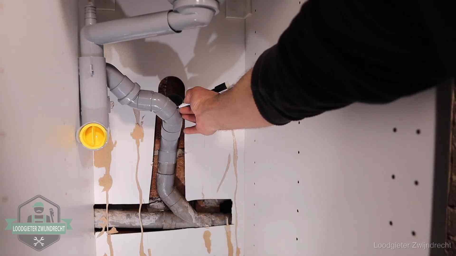Loodgieter markeert een pvc-afvoerbuis onder een gootsteen in Zwijndrecht