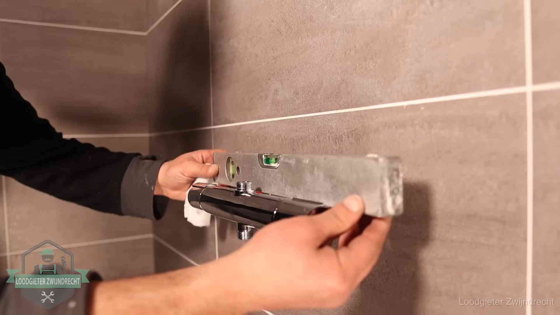 Loodgieter lijnt een douchekraan uit met een waterpas in een woning in Zwijndrecht