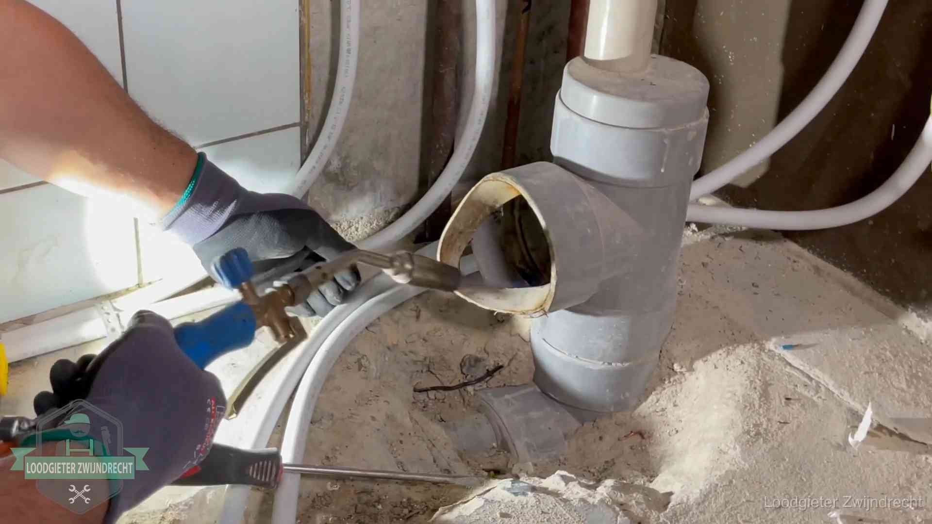 Loodgieter werkt met brander en messing kraanwerk aan leidingen in Zwijndrecht