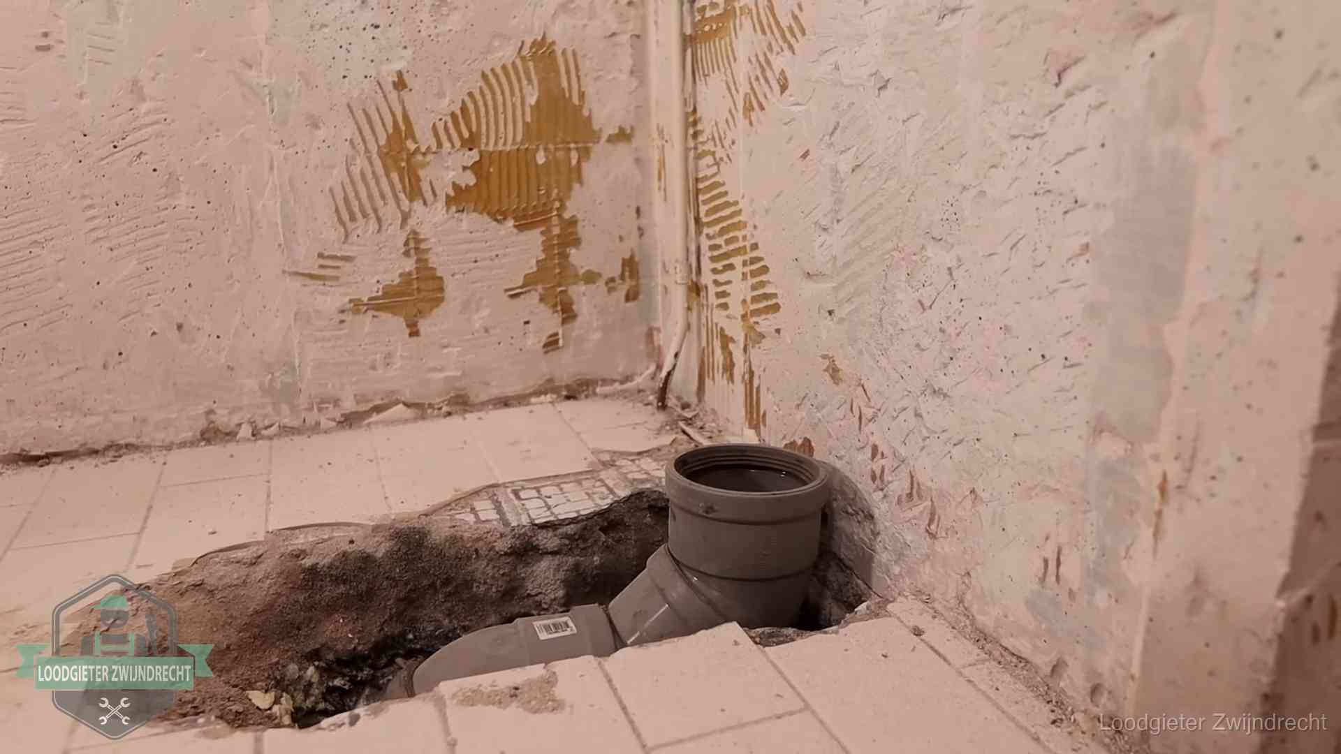 Verzakt riool herstellen in Zwijndrecht Opengebroken vloer met een nieuwe pvc-rioolbocht in een gegraven sleuf in Zwijndrecht