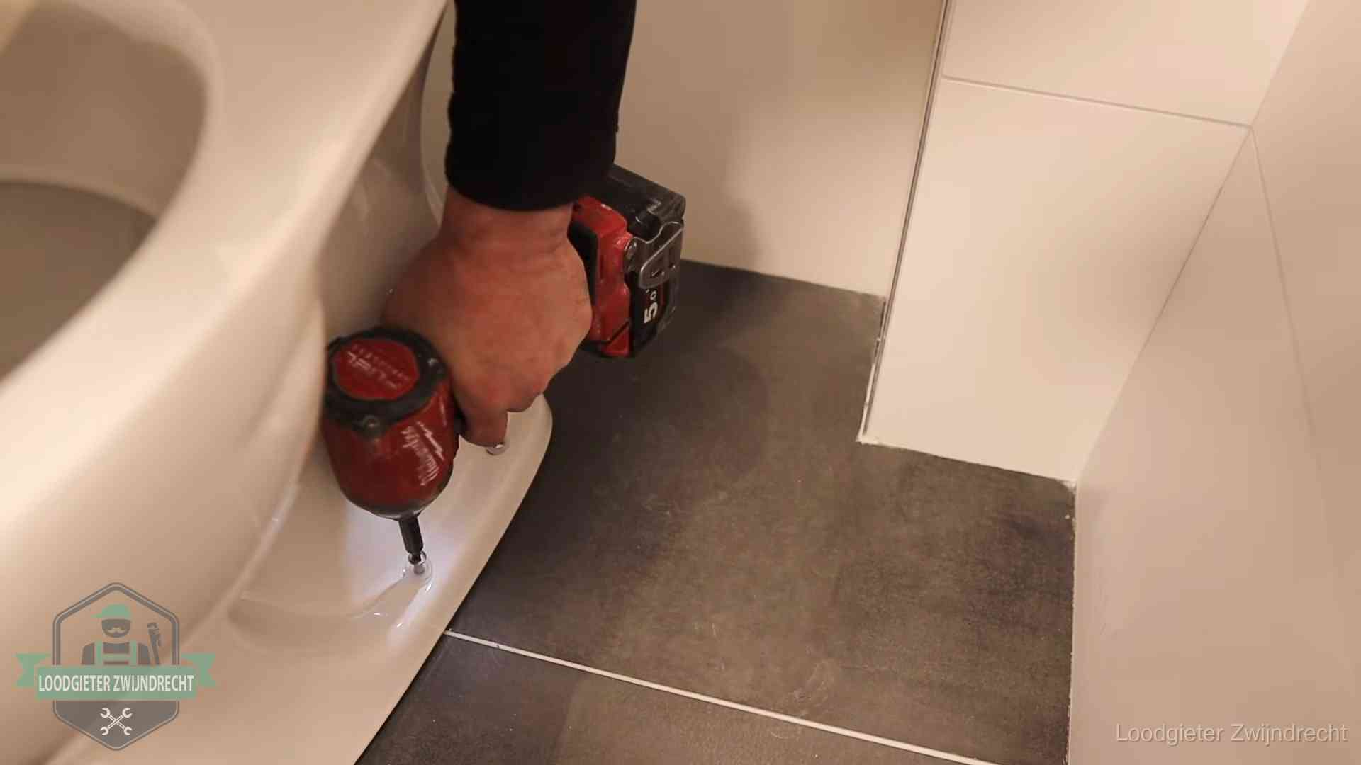 Kosten wc ontstoppen in Zwijndrecht Loodgieter zet de voet van een wc-pot vast op de tegelvloer in Zwijndrecht